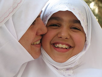 Close-up portrait of smiling mother and daughter in white hijabs
