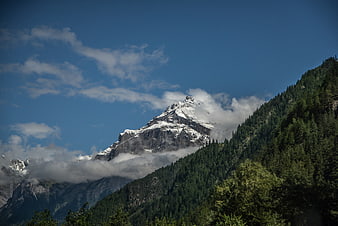 Snowy Alpine Peak with Clouds and Forest