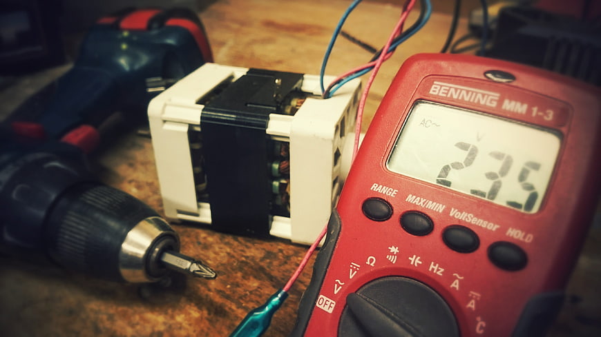 Red multimeter measuring voltage on workbench with drill