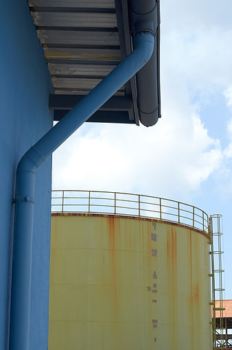 Blue industrial pipe and yellow storage tank against blue sky