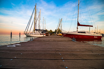 Sailboats docked at wooden pier during sunset
