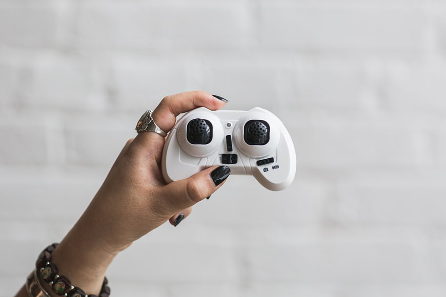 Woman's hand holding white game controller against white brick wall