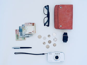 Flat lay of travel essentials, cash, camera, and accessories on white