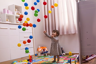 Toddler girl reaching for colorful floating balls in a bright nursery