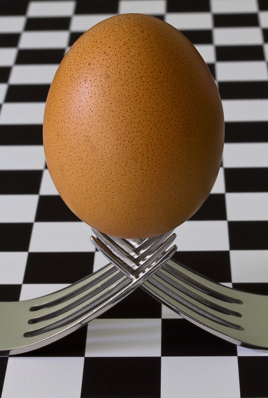 Brown egg balanced on crossed forks against checkered background