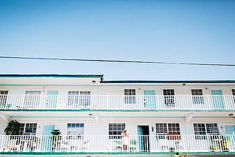 Woman standing on balcony of pastel motel under blue sky