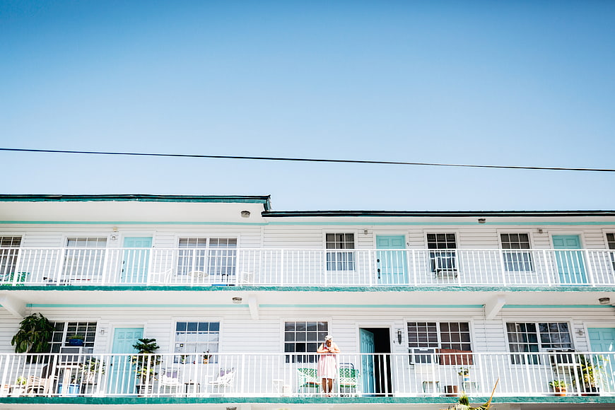 Woman standing on balcony of pastel motel under blue sky