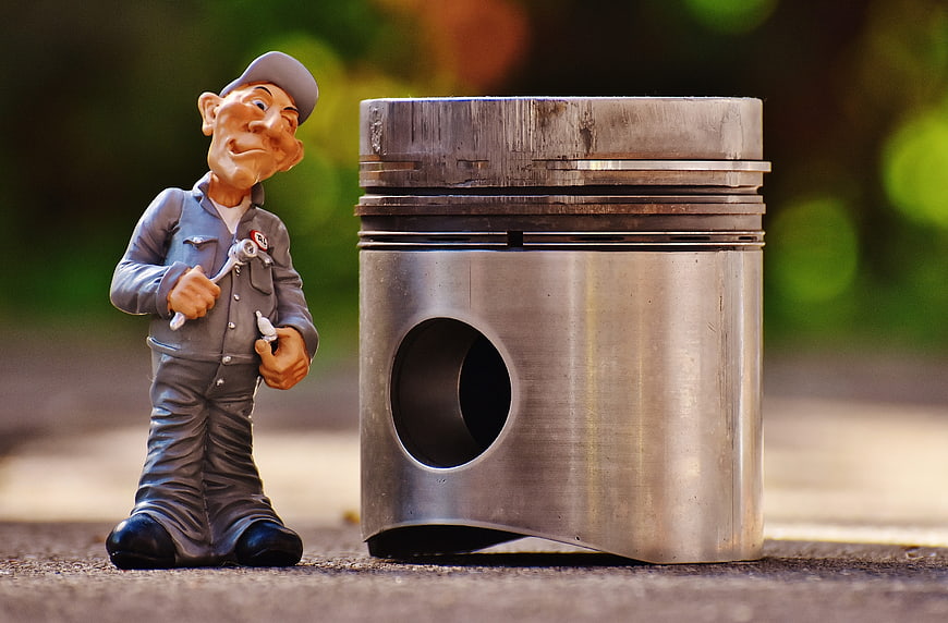 Mechanic Figurine Standing Next To Large Engine Piston
