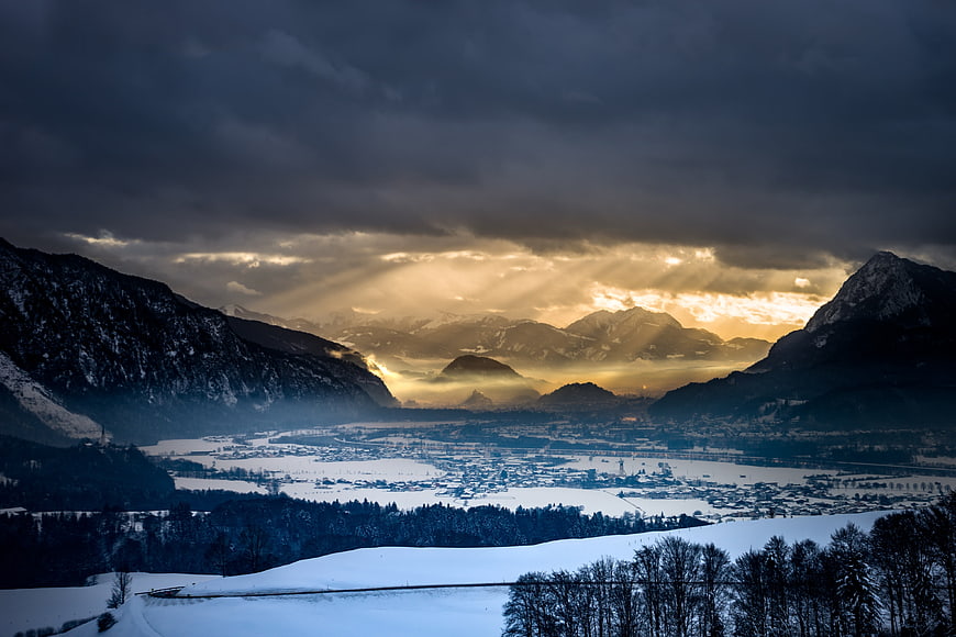 Dramatic Winter Alpine Valley Landscape With Sunbeams Breaking Through Dark Clouds