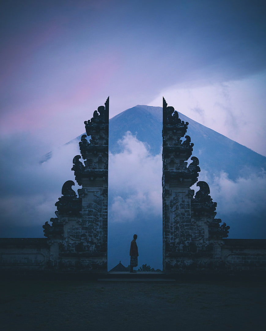 Silhouette of Man Standing in Balinese Temple Gate Framing Volcano