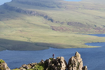 Hiker standing on rocky cliff overlooking vast green highland landscape and blue loch