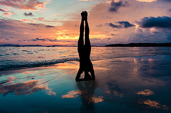 Silhouette of a person doing a yoga headstand on a beach at sunset