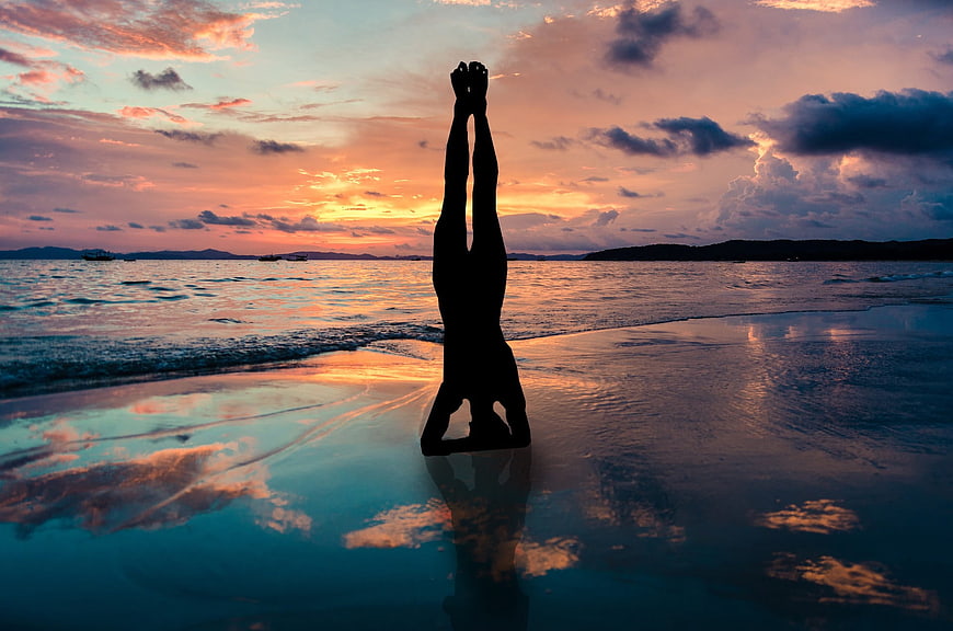 Silhouette of a person doing a yoga headstand on a beach at sunset