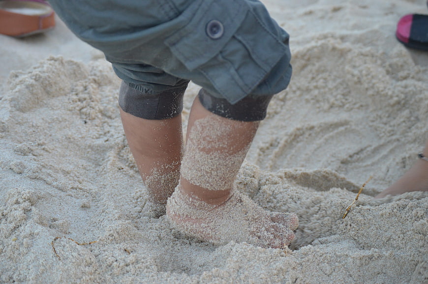 Close-up of baby legs playing in sand at the beach