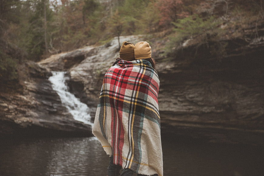 Couple wrapped in plaid blanket watching waterfall in autumn