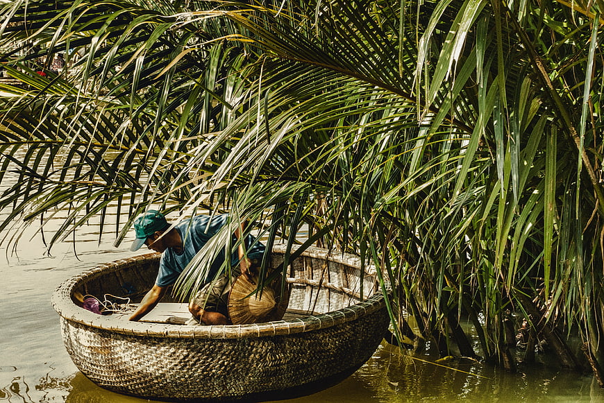 Man in traditional basket boat under palm leaves