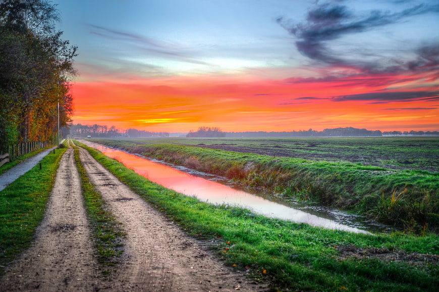 Vibrant sunset over rural canal and dirt road