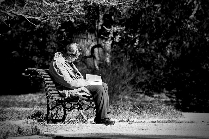 Senior man reading a book on a park bench in black and white