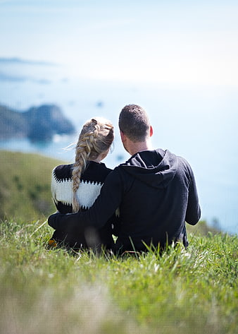 Couple sitting on grassy hill overlooking ocean view