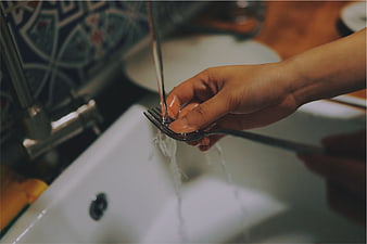 Close-up of hands washing a fork under running water in a kitchen sink