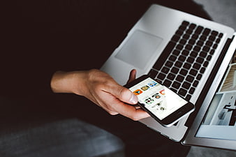 Hand holding smartphone over laptop keyboard workspace
