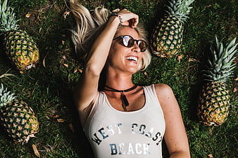Blonde Woman Lying on Grass with Pineapples