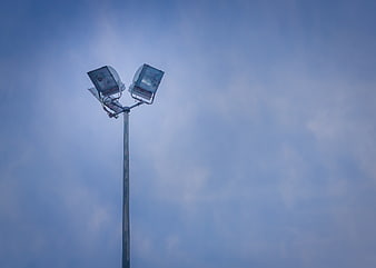 Dual floodlights on a pole against a cloudy blue sky