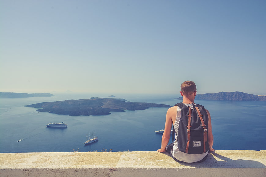 Backpacker Man Sitting on Wall Overlooking Santorini Caldera