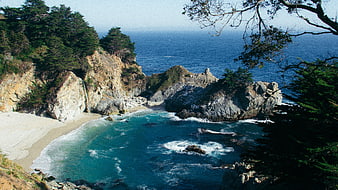 Scenic coastal cove with waterfall, sandy beach, and rocky cliffs