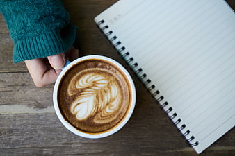 Overhead view of latte art coffee cup and notebook on wooden table