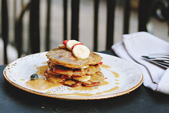 Stack of pancakes with banana, strawberry, and caramel sauce on a plate
