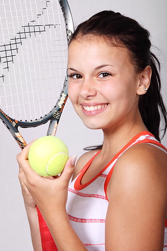 Smiling young woman holding tennis racket and ball
