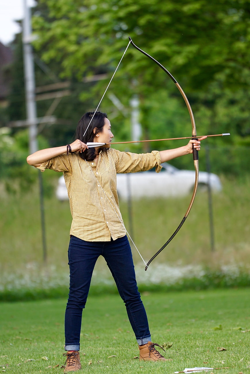 Woman practicing archery with traditional bow in a green park