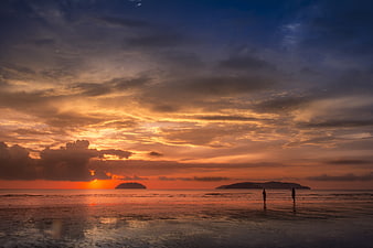 Dramatic Sunset Over Beach With Silhouetted Figures And Distant Islands