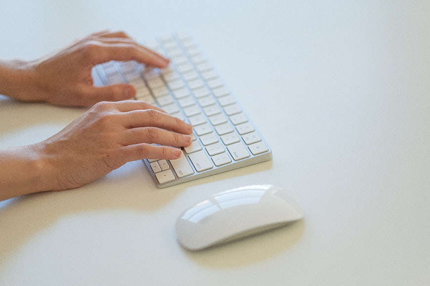 Hands typing on white keyboard and mouse on desk