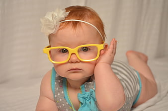 Adorable baby girl wearing oversized yellow glasses and a white flower headband