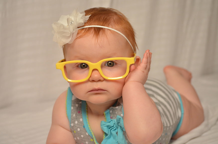 Adorable baby girl wearing oversized yellow glasses and a white flower headband