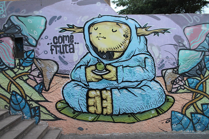 Colorful street art mural of a meditating character eating fruit