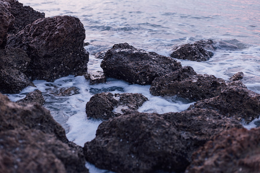 Dark volcanic rocks with ocean waves at sunset