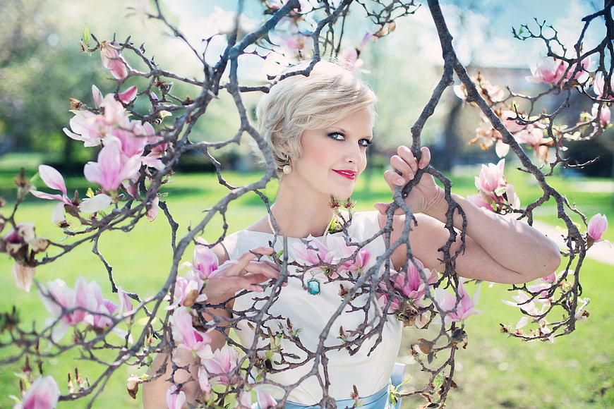 Blonde Woman Posing Among Pink Magnolia Blossoms