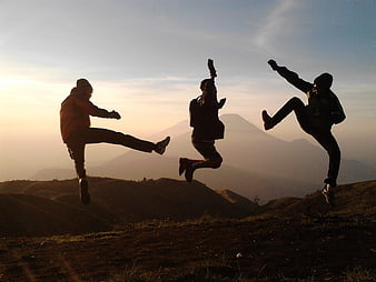 Three friends jumping in silhouette on a mountain ridge at sunset
