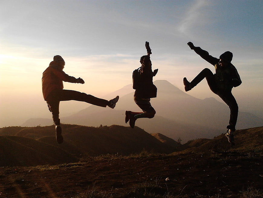 Three friends jumping in silhouette on a mountain ridge at sunset