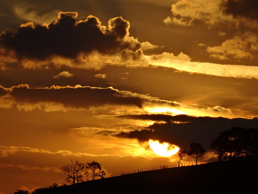 Dramatic golden sunset over silhouetted rolling hills and trees