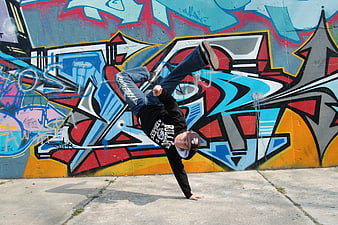 Breakdancer performing handstand against colorful graffiti wall