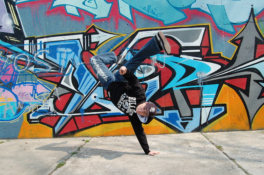 Breakdancer performing handstand against colorful graffiti wall