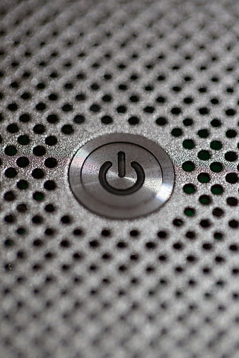 Close-up of a silver power button on a perforated metal surface
