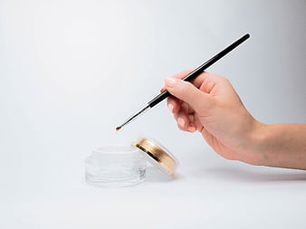 Hand applying gel polish with brush to jar on white background