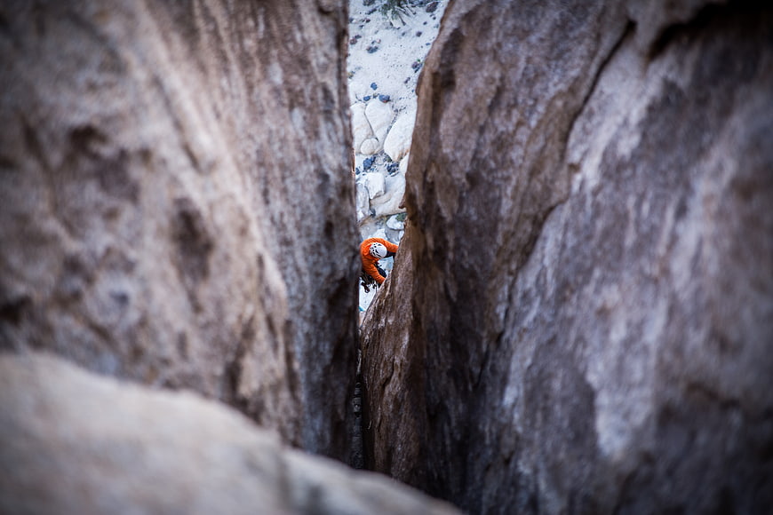 Rock climber squeezing through narrow canyon crevice