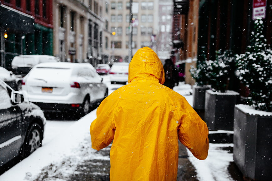 Person in Yellow Raincoat Walking in Snowy City Street