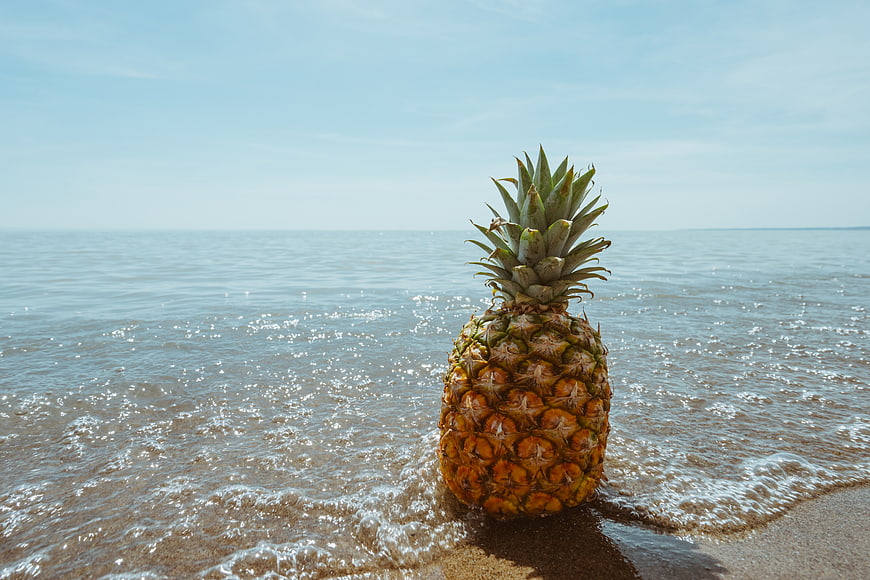 Fresh pineapple on sandy beach with ocean waves